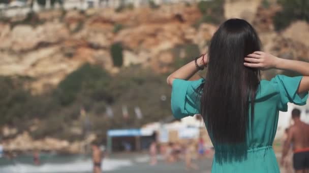 Mooi meisje met donkere haren, zonnebril, het dragen van een transparante jurk en een bikini op het strand draaien rond loopt. Schattige baby is genieten van een vakantie in het resort. Slow motion. — Stockvideo