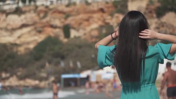 Bella ragazza con i capelli scuri, occhiali da sole, indossa un abito trasparente e un bikini cammina sulla spiaggia girando intorno. Bambino carino sta godendo una vacanza al resort. Rallentatore . — Video Stock