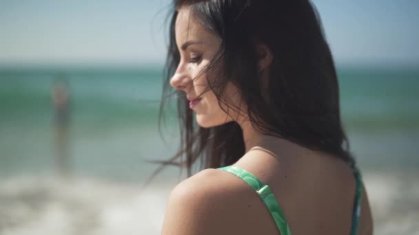 Mooi portret gelukkig smilling meisje permanent op de achtergrond van de zee. Gezicht van de mooie jonge vrouw met lang donker haar status in de zon. — Stockvideo