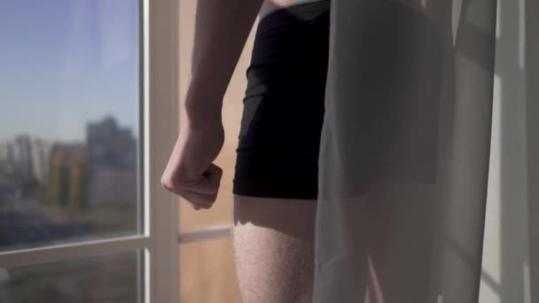 Мужчина в нижнем белье стоит за прозрачным тюлем возле большого окна в спальне . — стоковое видео