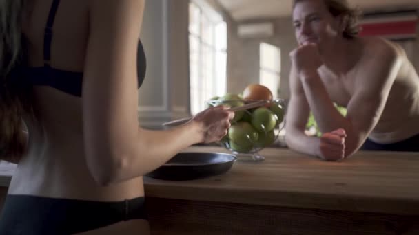 Jeune couple nu dans la cuisine du loft. Fille en lingerie donner cuillère vide pour son homme pour essayer de manger et l'homme agir comme son savoureux . — Video