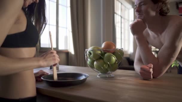 Jeune couple nu dans la cuisine du loft. Fille en lingerie cuisine demain dans une poêle interférer avec la nourriture avec une cuillère en bois . — Video