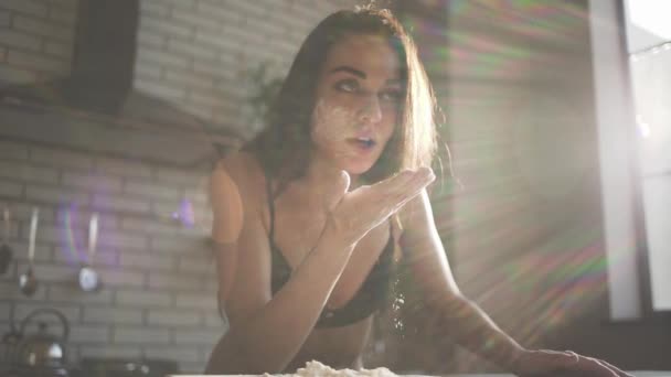 Brunette blow wheat flour in the air. Playful happy girl in lingerie with long brown hair standing in the morning sun cooking in the kitchen. Slowmotion shot. — Stock Video