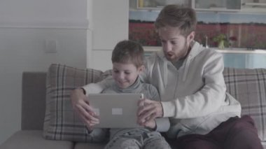 Gülümseyen mutlu baba ve çocuk dijital tablet büyük oturma odasında kanepede oturan kullanma. Baba oğluna öğretir. Aile birlikte vakit geçirmek. Baba-oğul ilişkisi.