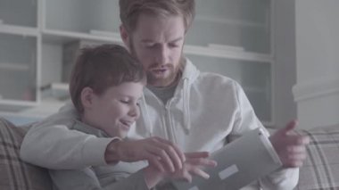 Baba ve oğul dijital tablet salonda kanepede oturan kullanma sakallı. Mutlu aile birlikte vakit geçirmek. Baba çocuğunu aracını kullanabilmek için öğretir. Baba-oğul ilişkisi.