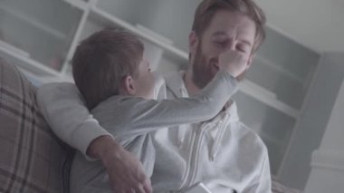 Baba ve küçük oğlu birbirlerine oturma odasında kanepede otururken burun çekme. Baba ve çocuk dostu ilişkisi. Baba-oğul ilişkisi.