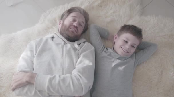 Happy lachende vader en zoon vreugdevolle liggen op het tapijt bont. Vader-kind relatie. Vader-kind relatie. — Stockvideo