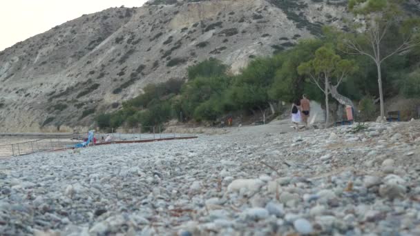 Dos personas caminan a lo largo de la costa del mar cerca de un acantilado montañoso después de ejercicios matutinos y tratamientos de agua — Vídeos de Stock