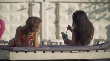 İki güzel kız arkadaşım güzel mayo kokteyler ile neşeli salonda üzerinde yüzme havuzu görüşme