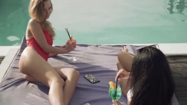 Tatlı bir sarışın ince bacakları ile neşeli diyalog güzel esmer ile salonda yakınındaki açık yüzme havuzu vardır. İki seksi kız arkadaşım boş mayolar.