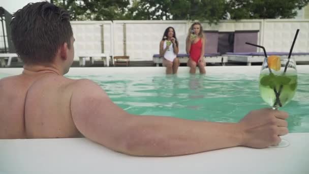 Rückansicht von feuchten jungen Mann aus dem Freibad auf dem Hintergrund von zwei schönen Mädchen. Gesellschaft von Freunden verbringt Freizeit im Schwimmbad. — Stockvideo