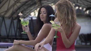 İki ince güzel kızlar kokteyler içme gözlük tıklatın ve lounge birlikte iyi vakit geçiriyoruz. İki seksi kız arkadaşım mayolar eğlence var.