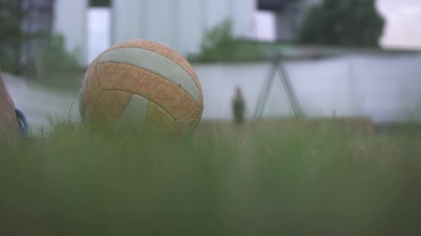 Close up view of volleyball ball on the green grass kicked by males foot to girl opposite. Slow motion. — Stock Video