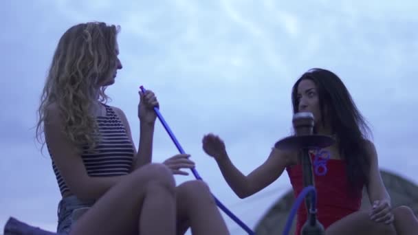 Två vackra flickor på kvällen rök vattenpipa, leende, dansa och ha en goot tid tillsammans utomhus på loungen — Stockvideo