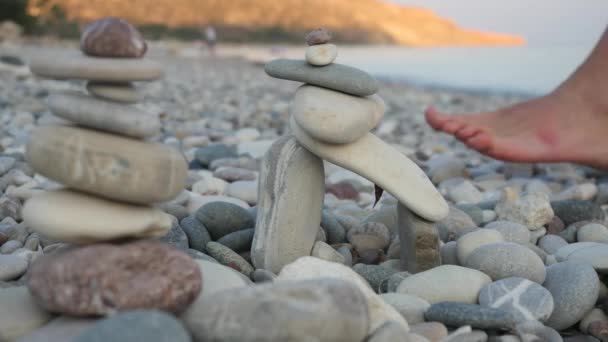 Männerbeine, die an einem steinigen Strand vor dem Hintergrund von Kieselsteinpyramiden spazieren gehen. verschwommene malerische Mittelmeerküste am Morgen — Stockvideo