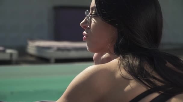Profiel portret van volwassen modieuze vrouw liggen in de buurt van zwembad. Vrije tijd van schattige dame in een bikini en zonnebril liggend op een ligstoel. — Stockvideo