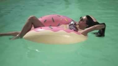 Genç ve güzel kadın güneş gözlüğü üzerinde pembe Kauçuk halka yalan havuzu yüzme güneş sahiptir. Bir bikini yalnız kadın eğlence.