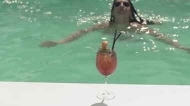 Pembe Kokteyl havuz tarafında duruyor. Kadın cam ve içki içmek için gidiş için yüzüyor. Eğlence güzel Bayan.