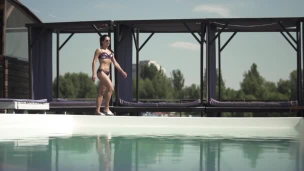 Mujer morena en traje de baño de plata brillante en caminatas cuerpo atlético cerca de la piscina. Ocio de dama solitaria en bikini . — Vídeo de stock