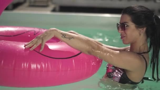 Brünette Frau mit Sonnenbrille hält rosa Gummiring im Wasser eines Swimmingpools. Freizeit einsamer Dame im Bikini. — Stockvideo