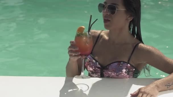 Mooie vrouw in zonnebril is het drinken van haar cocktail staande in zwembad. Vrije tijd van eenzame dame in een bikini. — Stockvideo