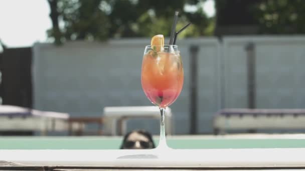 Nærbilde av en cocktail på kanten av et svømmebasseng i bakgrunnen av sprutende vann med blanke gnister . – stockvideo