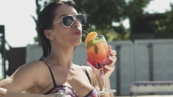 Fröhlich lächelnde Frau mit Sonnenbrille, die ihren Cocktail trinkt. Freizeit einsamer Dame im Bikini. — Stockvideo