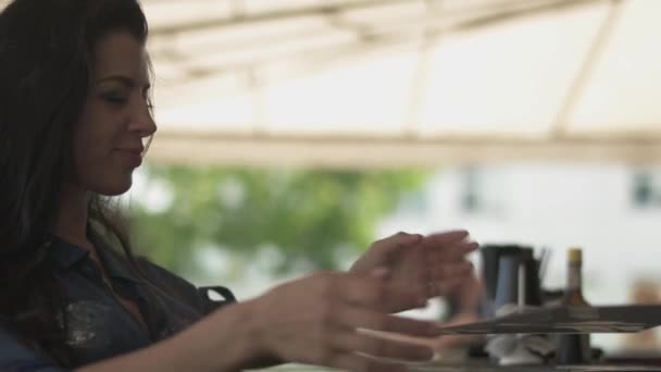 Cute nice woman looking menu in the restaurant and correcting her hair. Lonely girl resting in a cafe. — Stock Video