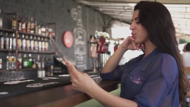 Ganska ung kvinna ser menyn i restaurangen och korrigera hennes hår. Ensam flicka vilar i ett café. — Stockvideo