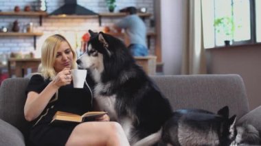 Kadın kanepede oturuyor okur bir kitap, içecekler kahve ve görüşmeler husky süre kocasını mutfakta bir şey pişiyor