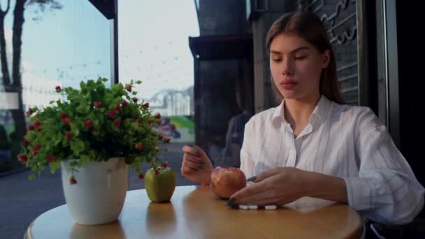 La ragazza getta via le pillole vitaminiche con la mano dal tavolo e mangia una deliziosa mela verde seduta sulla terrazza di un caffè all'aperto — Video Stock