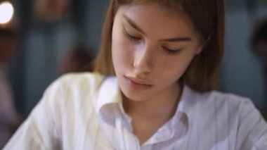 Dudaklar bir kalemin tutan bir kafede oturan beyaz gömlekli genç bir kızın portresi. Kız yazıyor sonra etrafına bakıyor ve yaprakları.