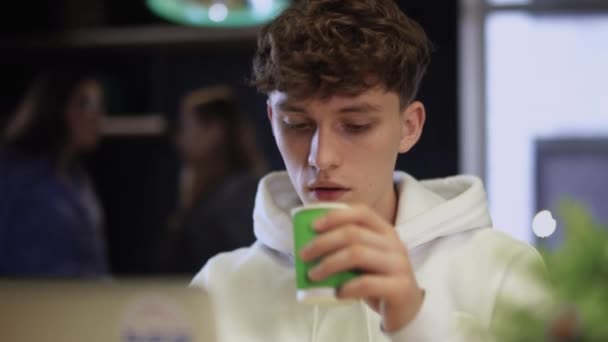 Portret van jonge gerichte kerel werken voor een laptop en het drinken van koffie uit papier beker — Stockvideo