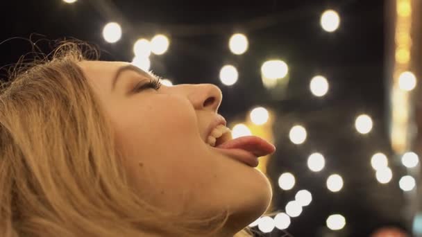 Close-up of joyful female face catching snowflakes with her mouth popping out her tongue. Cute girl has fun in the winter outdoors — Stock Video