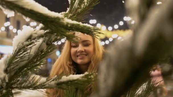 Menina alegre feliz perto do ramo de abeto na neve Os galhos de árvore de Natal com a neve estão em primeiro plano . — Vídeo de Stock