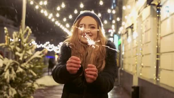 Portret van jonge lachende vrouw met wonderkaarsen in handen buitenshuis. Sparks verstrooit in verschillende richtingen — Stockvideo