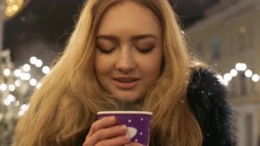 Bir kış ceket bir kış sokakta duran ve karton bardak sıcak çay onun elinde tutan uzun sarı saçlı güzel güleryüzlü genç kız portresi.