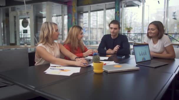Neljä nuorta aikuisyrittäjää keskustelee uusista strategioista startup-yrityksissä käyttäen kannettavia tietokoneita modernissa yhteistyössä suurkaupungissa — kuvapankkivideo