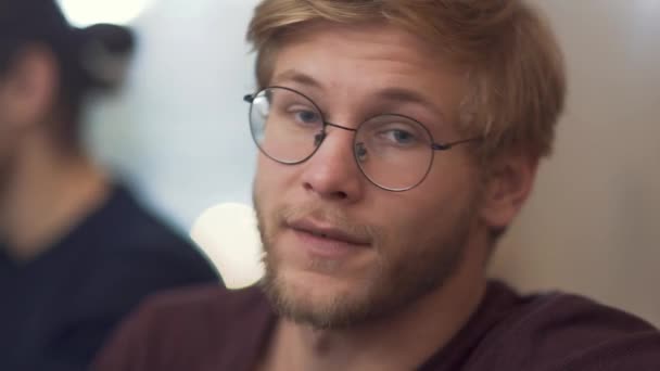 Bearded guy with glasses shares his impressions conveying his emotions from the meeting at the discussion table with his partners. — Stock videók