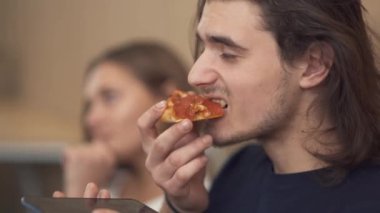 Genç sakallı biri sandviç yemeyi ve cep telefonuyla konuşan portresi