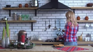 Cute mother in plaid shirt with long blond hair cooking breakfast and small naughty girl bite one cookie