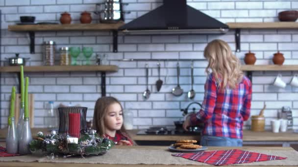 Hübsche Mutter im karierten Hemd mit langen blonden Haaren kocht Frühstück und kleines Mädchen beißt in einen Keks — Stockvideo