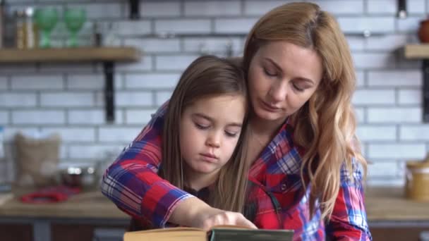 Güzel genç anne mutfak masada oturan sevimli küçük kızım için bir kitap okuma. Çocuk üzgün ve anneme dinlemek istemiyor — Stok video