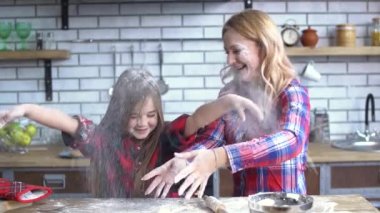 Carefree beautiful young mother and daughter fooling in the kitchen. Mom and child have fun together.