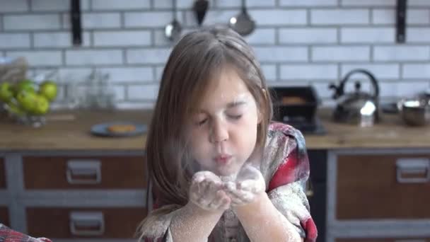 Portrait of a little girl heavily soiled in flour blowing flour from her palm. Cute girl having fun in the kitchen. — Stock video