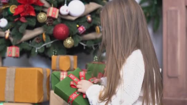 Petite fille mignonne avec de longs cheveux bruns assis près de l'arbre de Noël et des cadeaux ouverts — Video