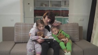 Mutlu anne ve iki çocuğu kanepede oturuyor. Kadın çocuk için tablet gösterir. Aile tatilleri.