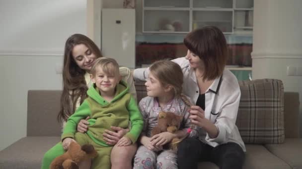 Due sorridenti sorelle maggiori e una divertente sorella minore e fratello seduti sul divano nella stanza degli ospiti. Felice vacanza in famiglia . — Video Stock