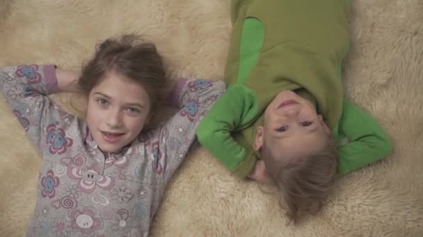 Adorables niños pequeños en pijama tumbados en el suelo con alfombra esponjosa. Hermano y hermana juntos. Feliz fin de semana de hermanos . — Vídeos de Stock