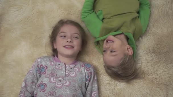 可爱的孩子穿着睡衣躺在地板上蓬松的地毯。兄妹在一起玩得很开心。愉快的兄弟姐妹周末. — 图库视频影像